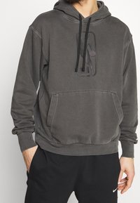 Grauer Kapuzenpullover aus Baumwolle mit einer vorderen Kängurutasche und einem dezenten, geprägten Logo. Strukturiertes Material mit lässiger Passform.