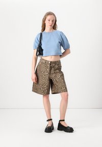 Ljusblå cropped denim-top med puffärmar, matchad med leopardmönstrade shorts och svarta platåskor, samt en liten svart handväska.