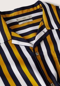 Camisa de manga corta con rayas verticales en azul marino, mostaza y blanco. Hecha de tela suave, con bolsillo en el pecho y diseño con botones.