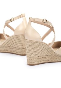 Sandales compensées en cuir beige avec une plateforme en jute texturé, dotées d'une sangle de cheville croisée sécurisée par une boucle en or.