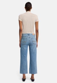 Ljusbeige kortärmad topp parat med högmidjade, avsmalnande ljusblå jeans med fransade fållar och bakfickor med sömdekoration.