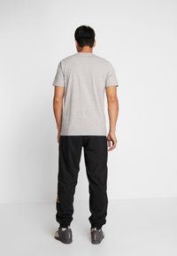 Grå t-shirt med kort ärm och rund halsringning, kombinerad med svarta träningsbyxor med en guldig logotyp, och gråa sportskor.