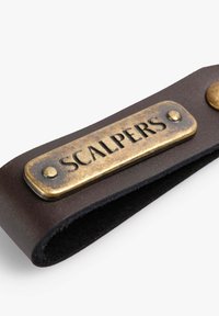 Correa de muñeca de cuero en marrón oscuro con una placa de latón vintage que dice "SCALPERS", acentuada por un botón redondo de latón. Acabado texturizado.