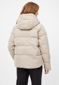 Beige pufferjack met een capuchon, voorzien van een geregen ontwerp, een gladde textuur en ribbelaccenten. De achteraanzicht toont een relaxte pasvorm.