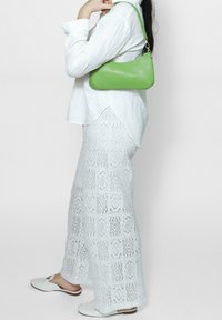 Pantaloni ampi bianchi in pizzo, borsa a spalla verde in pelle, camicia bianca con bottoni. La borsa presenta un materiale testurizzato, mentre i pantaloni hanno dettagli intricati e decorati.