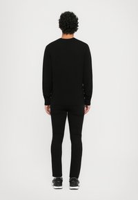 Μαύρη μακρυμάνικη φούτερ μπλούζα από μαλακό ύφασμα, με στρογγυλή λαιμόκοψη, ριμπ μανίκια και στρίφωμα, συνδ�υασμένη με στενά μαύρα παντελόνια και αθλητικά παπούτσια.