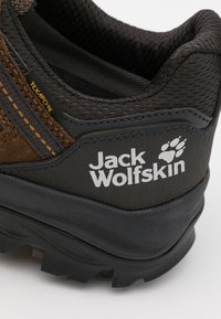 Braun- und grau gefärbter Schuh mit einer strukturierten Oberfläche, Gummisohle und auffälligem Jack Wolfskin-Logo. Enthält dezente orange Akzente und Designdetails.