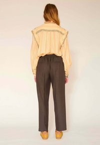 Blouse jaune à rayures avec col froncé associée à un pantalon marron. Le pantalon dispose d'une ceinture élastique et de deux poches arrière.