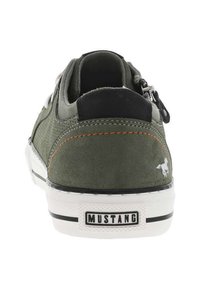 Sneaker verde in suede con una finitura texturizzata, dettagli neri e cuciture arancioni. Presenta una suola bianca e un logo del brand ben visibile sul tallone.