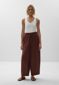 White fitted tank top, loose burgundy wide-leg pants with an elastic drawstring waist, and brown flip-flops, standing against a neutral background.