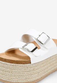 Sandali platform bianchi con suola in juta testurizzata, dotati di due fibbie argentate regolabili su ampie cinghie. Sottopiede liscio con una finitura naturale.