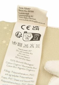 Etiket met wasinstructies op lichtbeige stof, met zwarte tekst en pictogrammen; bevat details over de stofsamenstelling en informatie over de fabrikant.