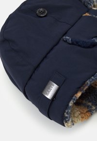 Navy blauwe wintermuts met een zachte, gestructureerde voering in tinten van crème, oranje en blauw. Voorzien van een zwarte knop en een zilveren merklabel.