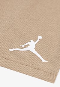 Un tissu beige avec une texture côtelée présente une silhouette du logo Jordan en blanc dans une pose athlétique, positionnée près du bord.