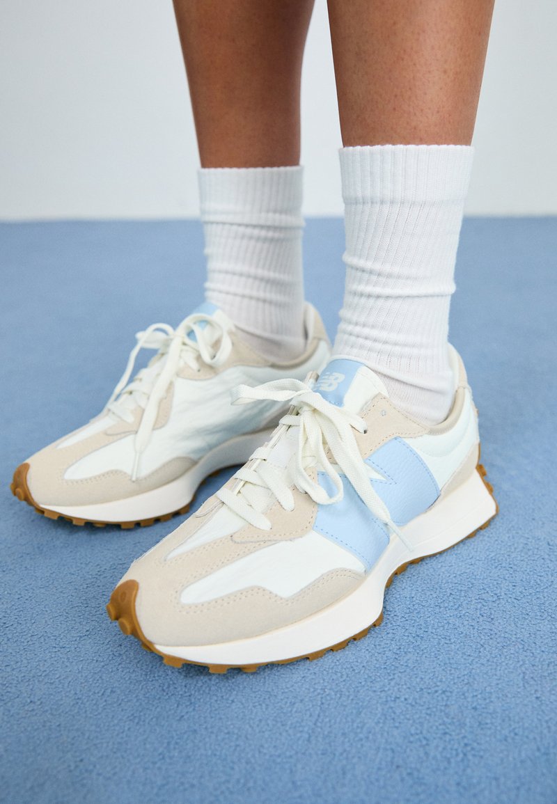 Sneakers leggeri con un design beige e azzurro chiaro. Presentano materiali in suede e mesh, lacci bianchi e suola in gomma testurizzata.