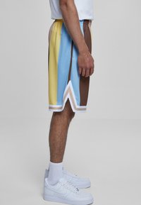 Košarkarske kratke hlače z navpičnimi črtami v modri, rumeni, rjavi in beli barvi, z elastičnim pasom in čevlonasto dekoracijo na robu.