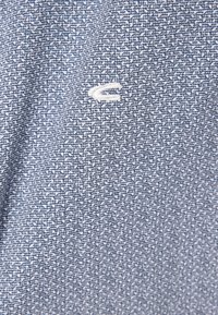 Blau gemusteter Stoff mit weißem abstraktem Design. Enthält ein kleines weißes Logo, das im unteren Abschnitt gestickt ist. Weiche Textur.