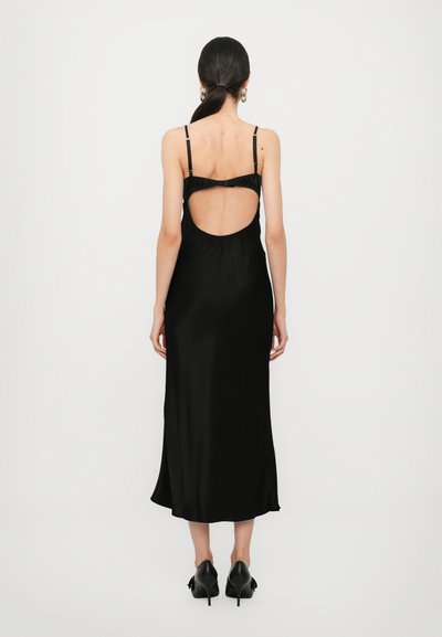 Vestido negro de satén con tirantes finos y espalda descubierta. Diseño de media longitud, textura suave y con un ligero acampanado en el dobladillo. Combinado con tacones negros.