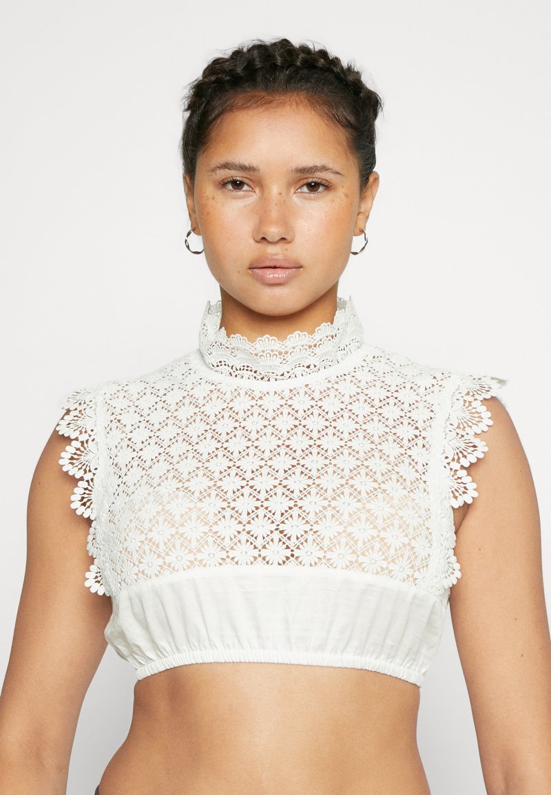 Weißes Crop-Top mit filigranem Spitzenmuster, floralem Design, hohem Kragen und elastischem Saum, das eine strukturierte Optik bietet.