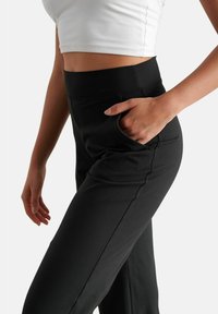 Pantaloni neri con vita alta, tasche laterali e un tessuto liscio e elasticizzato. Progettati per offrire comfort con una vestibilità affusolata.