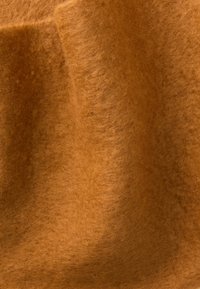 Materiale in feltro di lana marrone con una superficie morbida e texturizzata, caratterizzato da una tonalità calda e ricca e lievi variazioni di colore e profondità.