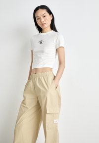 Witte cropped t-shirt met geborduurd logo en korte mouwen, gecombineerd met beige cargobroek met zijzakken en een elastische tailleband.