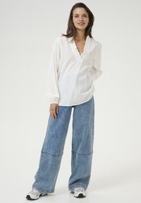 White long-sleeve blouse with a ruffled V-neck. Paired with wide-leg light blue denim jeans, featuring seam details and a relaxed fit.