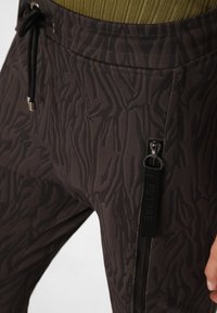 Dunkel gemusterte Jogginghosen mit strukturiertem Finish, ausgestattet mit einer seitlichen Zippertasche und einem verstellbaren Kordelzug für einen sicheren Sitz.