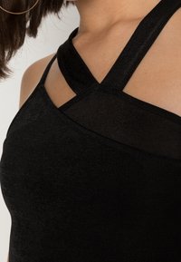 Svart ärmlös topp med en slät yta, med en asymmetrisk halsringning och korsande band som framhäver en figursydd design.