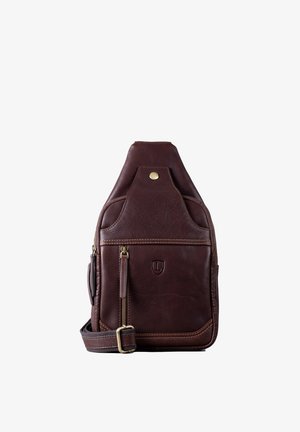 Braune Lederslingtasche mit abgerundetem oberen Ende, Messingbeschlägen, einer vorderen Reißverschlusstasche und einem Logo. Texturierte Oberfläche mit kontrastierenden Nähten.