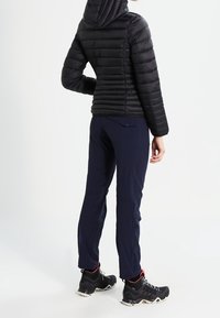 Zwarte gewatteerde jas met capuchon, marineblauwe broek en zwarte wandelschoenen. Heeft een gewatteerde textuur en een lichtgewicht ontwerp.