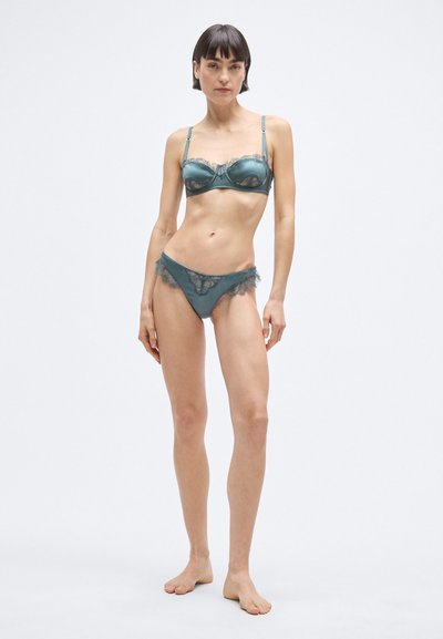 Súprava tyrkysovej čipkovanej podprsenky a nohavičiek. Podprsenka má priesvitný čipkový lem a nastaviteľné ramienka; nohavičky majú vlnité čipkové okraje. Hladká látka.