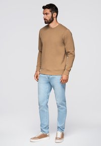 Felpa marrone con collo rotondo, jeans azzurri chiari e sneakers beige. La felpa ha una texture liscia; i jeans sono aderenti.