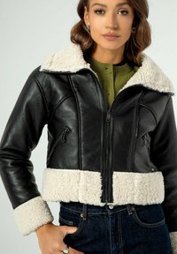 Giubbotto in pelle nera con collo e polsini in shearling bianco, dotato di chiusura a zip sul davanti e tasche laterali, con un design accorciato.