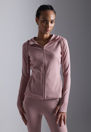 Light pink zip-up hoodie made of stretchy fabric, featuring a hood, long sleeves, and seamless detailing for a smooth finish.
