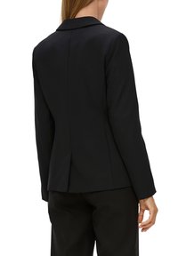 Schwarzer maßgeschneiderter Blazer mit Reverskragen, figurbetonter Passform, langen Ärmeln und einem einzelnen Rücken-Schlitz für mehr Bewegungsfreiheit. Glatte Stofftextur.