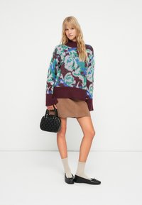 Maglione sovradimensionato a maglia con motivo floreale multicolore, bordato in bordeaux, abbinato a una gonna marrone. Gli accessori includono una borsa nera.