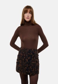 Un haut à col roulé marron associé à une mini-jupe noire brodée avec un motif floral, des accents de boutons et une finition texturée.