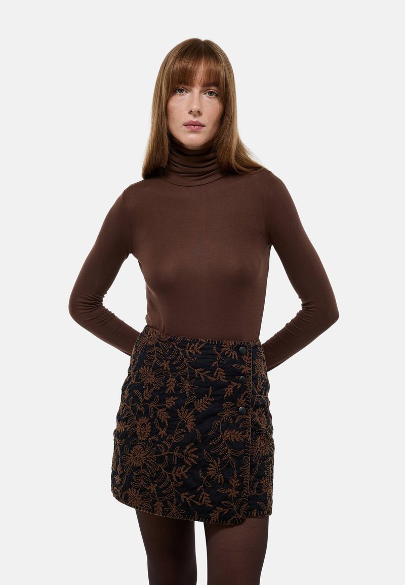 Un haut à col roulé marron associé à une mini-jupe noire brodée avec un motif floral, des accents de boutons et une finition texturée.