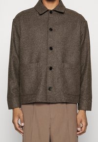 Braune Wolljacke mit Kragen, durchgehender Knopfleiste, zwei Seitentaschen und gerade geschnittenem, lockerem Sitz.