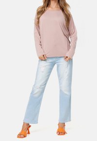 Helles rosa langärmliges Oberteil, verwaschene hellblaue Jeans und orangefarbene Fransen-Sandaletten mit hohen Absätzen. Legere Kleidung mit lockerer Passform und strukturierten Details.