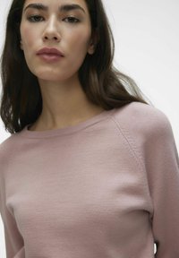 Ljusrosa tröja med rund hals, fin stickad textur och raglansärmar som visar subtila sömdetaljer. Mjuk tygfinish.