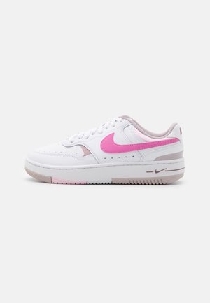 White leather sneaker with pink accents, textured toe, eyelets, and a cushioned sole. Features a rounded shape and raised heel.