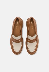 Zapatos de cuero marrón tipo slip-on con una superposición de tela crema, que cuentan con dobles correas y detalles de costura blanca. La marca Geox es visible en el interior.