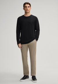 Maglietta nera a maniche lunghe, pantaloni beige, abbinati a sneaker nere. L'outfit è casual, con tessuto morbido e design rilassato.