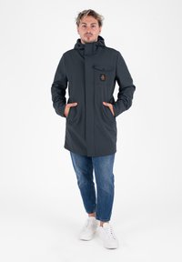 Donkergrijze hoodie met een voorzak. Kenmerkt zich door een ritsluiting, zijzakken en een nette snit. Gemaakt met blauwe jeans en witte schoenen.