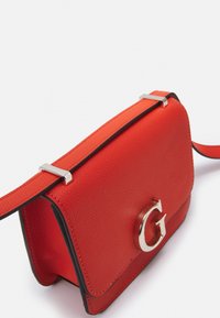 Rød læder skuldertaske med en struktureret design, sølv hardware og et fremtrædende G-logo på forsiden. Har en kontrasterende sort kant.