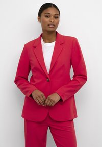 Blazer aderente rosa con revers a punta, chiusura a un bottone e una texture liscia, abbinato a una t-shirt bianca sotto.