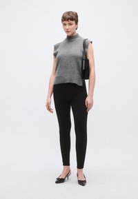 Pulover gri fără mâneci, tricotat, cu guler înalt, asortat cu colanți negri mulați și pantofi negri cu toc. Accesoriile includ o geantă mică neagră.