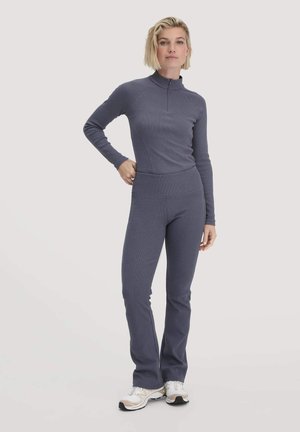 Enganliegender Zweiteiler für das Workout aus dunkelgrauem Stoff. Langärmliges Oberteil mit Reißverschlusskragen; ausgestellte Hose mit breitem elastischem Bund.